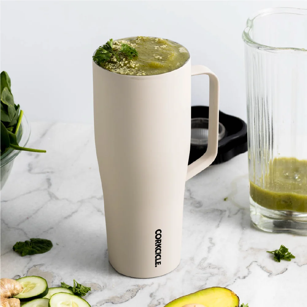 Vaso Corkcicle Cold Cup XL color latte sobre una mesada de mármol, junto a un licuado verde